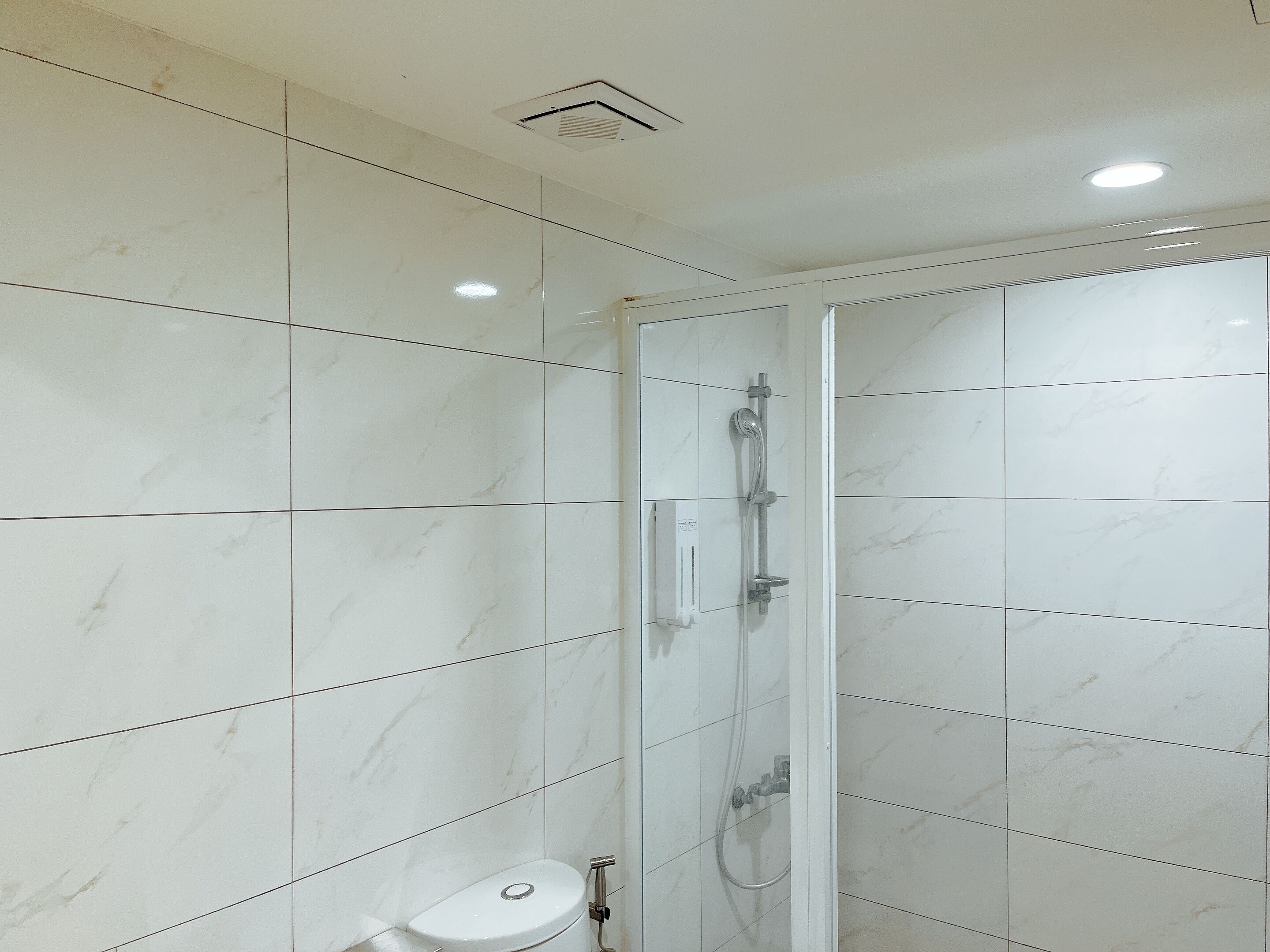 A modern bathroom with white marble tiles, a glass-enclosed shower, and a toilet.