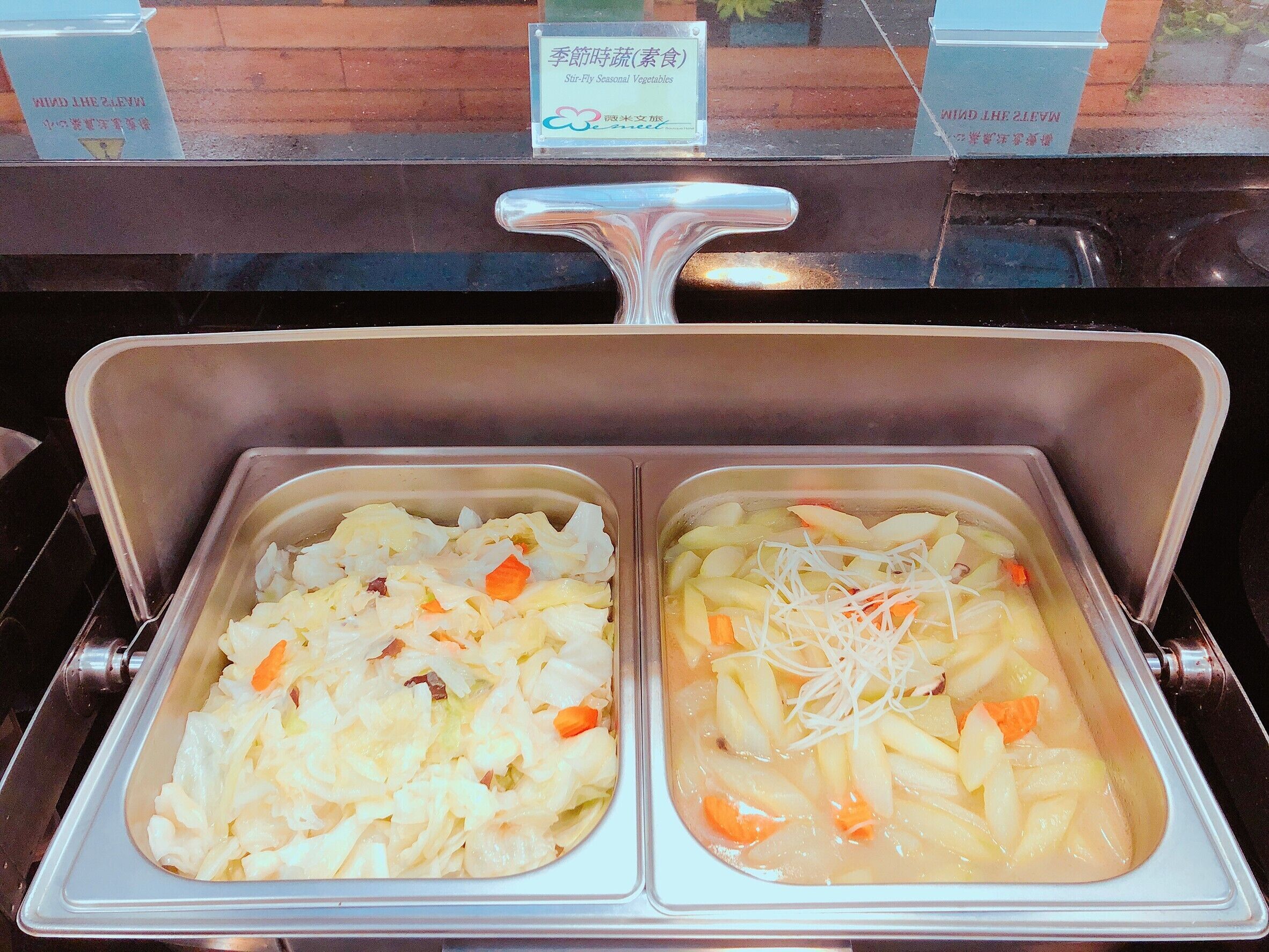 A buffet with two trays of food, one with cabbage and carrots and the other with noodles and carrots.