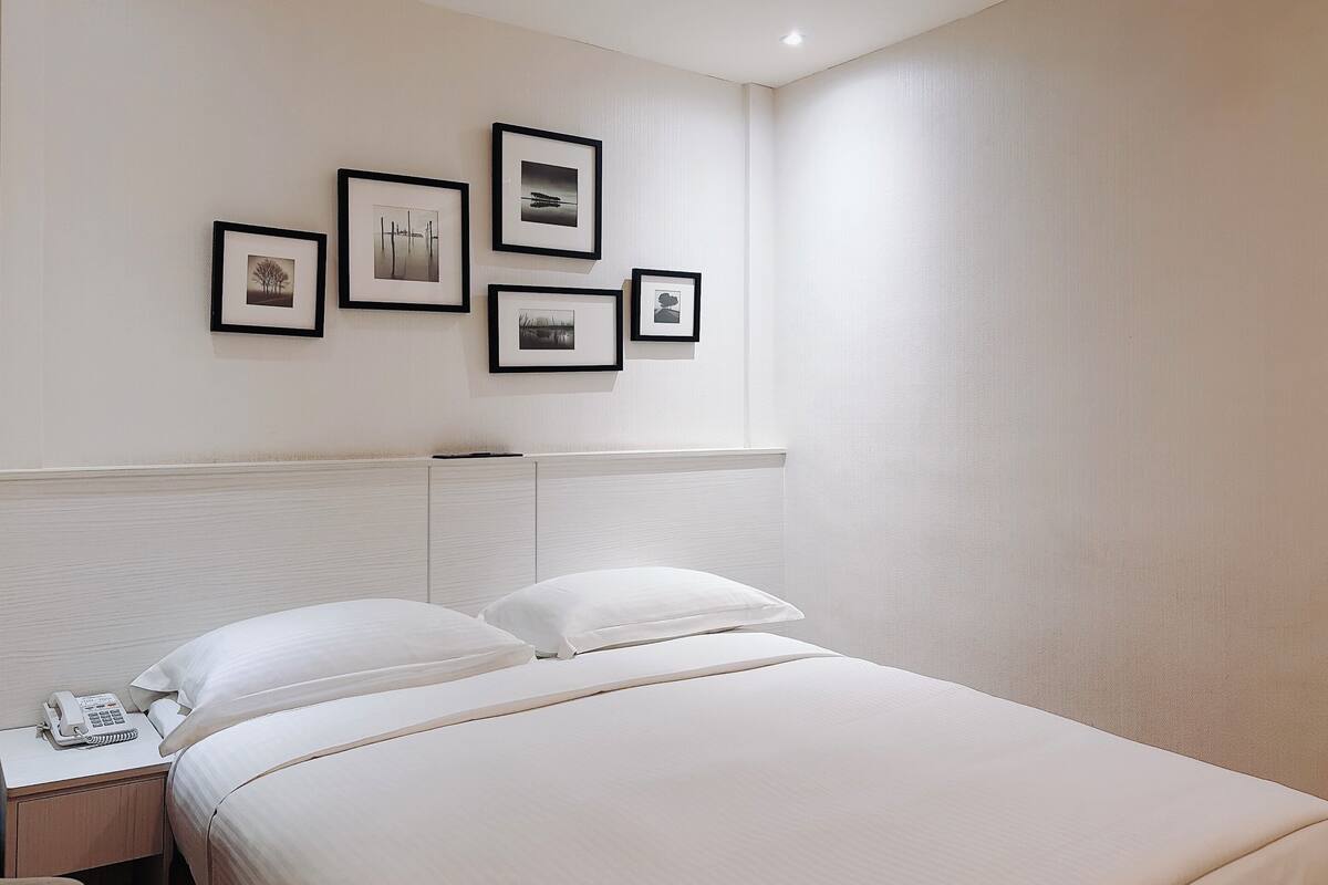 Habitación de hotel con una cama, una mesita de noche con teléfono y una pared decorada con cuadros.