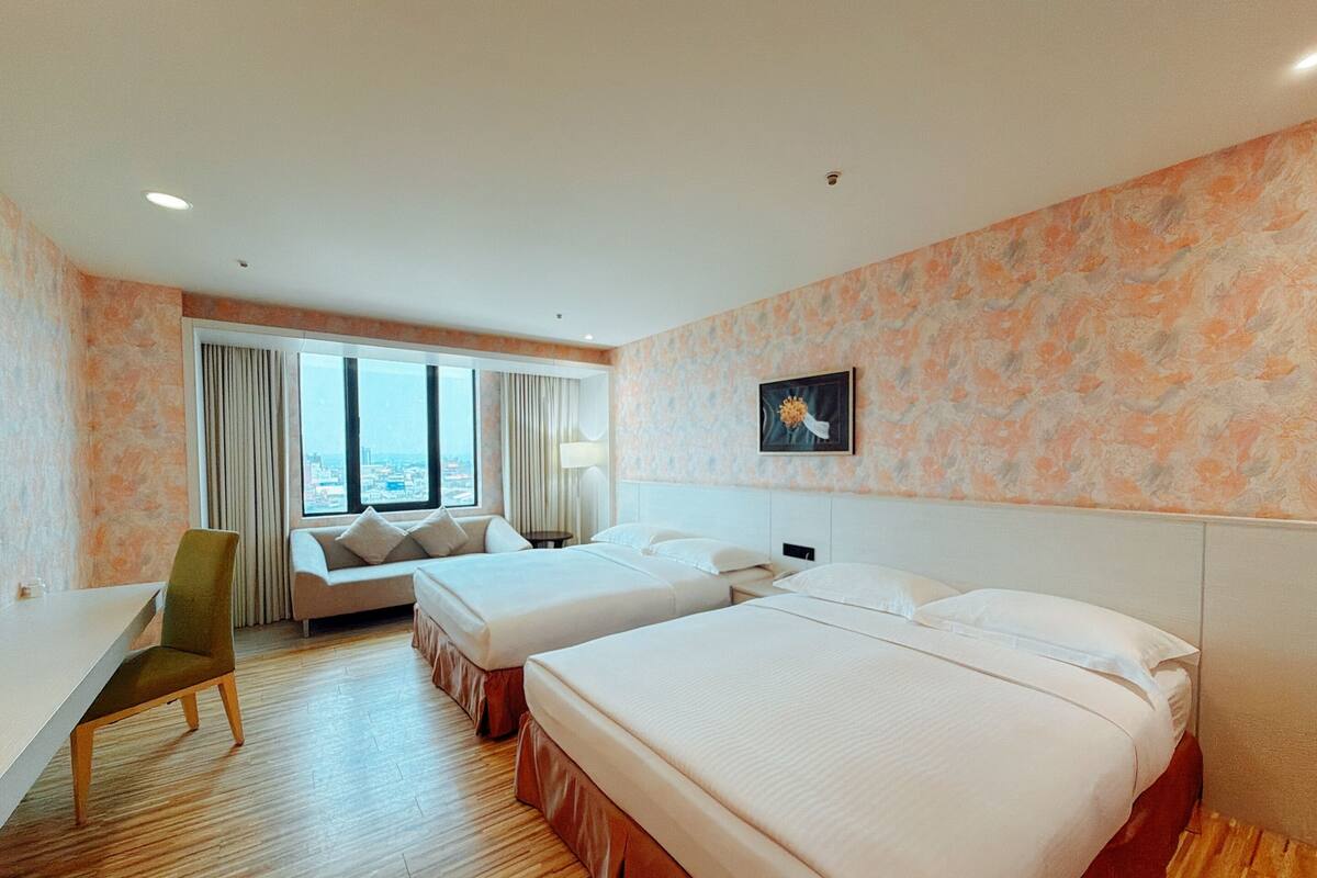 Habitación de hotel con dos camas, un escritorio, una silla y un amplio ventanal con vistas a la ciudad.