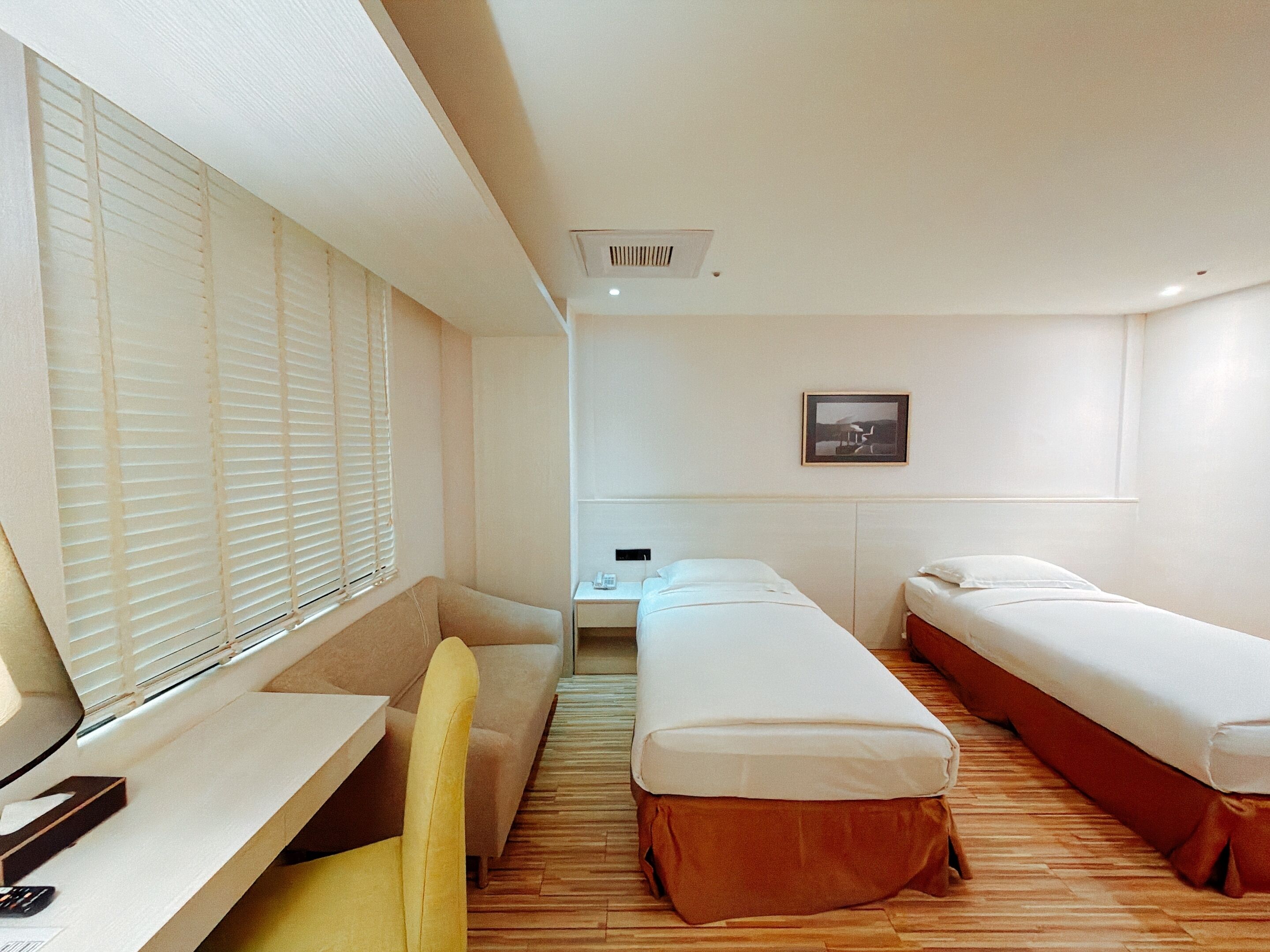 Ein Hotelzimmer mit Schreibtisch, zwei Einzelbetten, einer Couch und einem Fenster mit Jalousien.