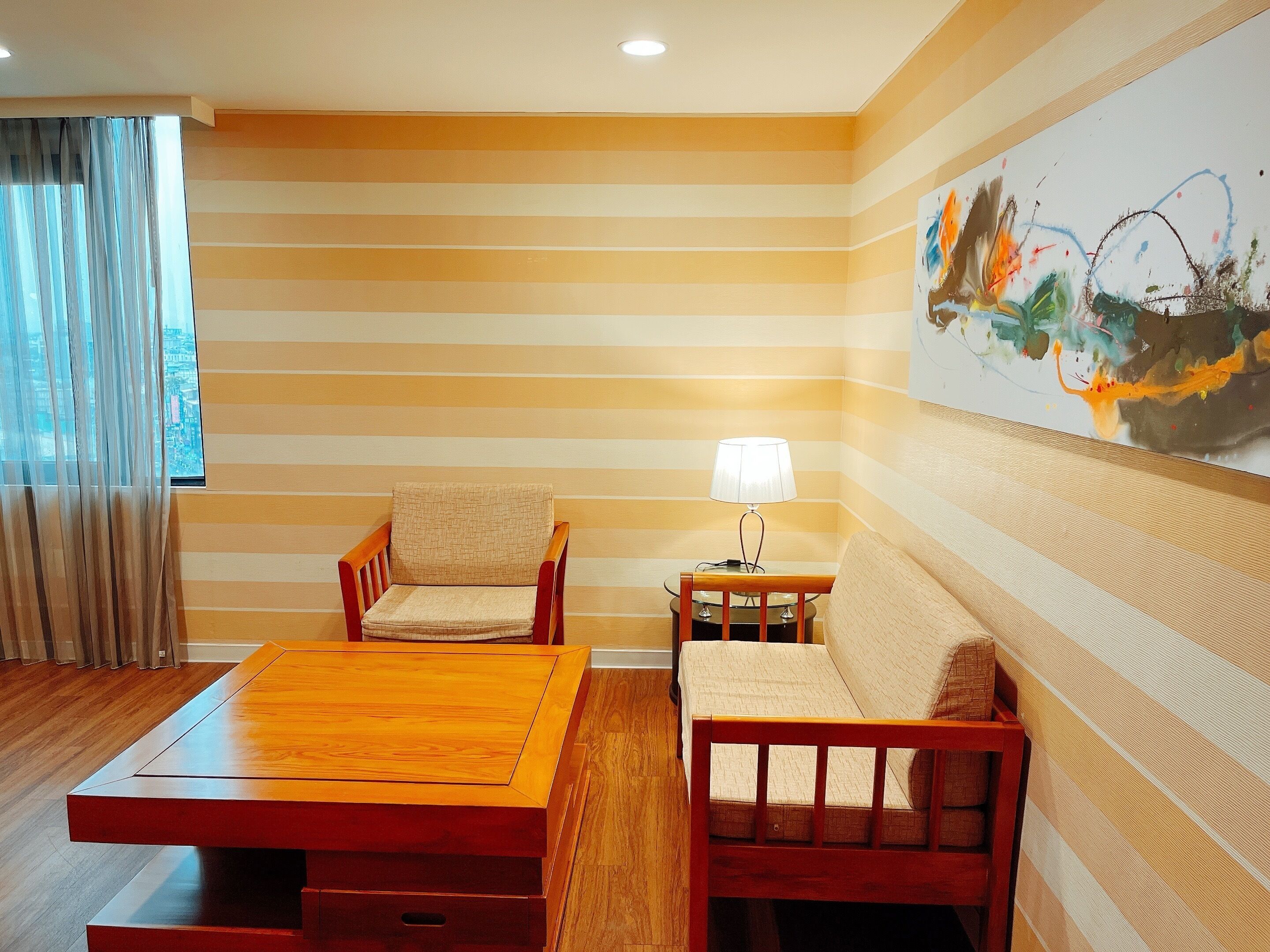 A room with a striped wall, a wooden table with chairs, a lamp, and a painting.