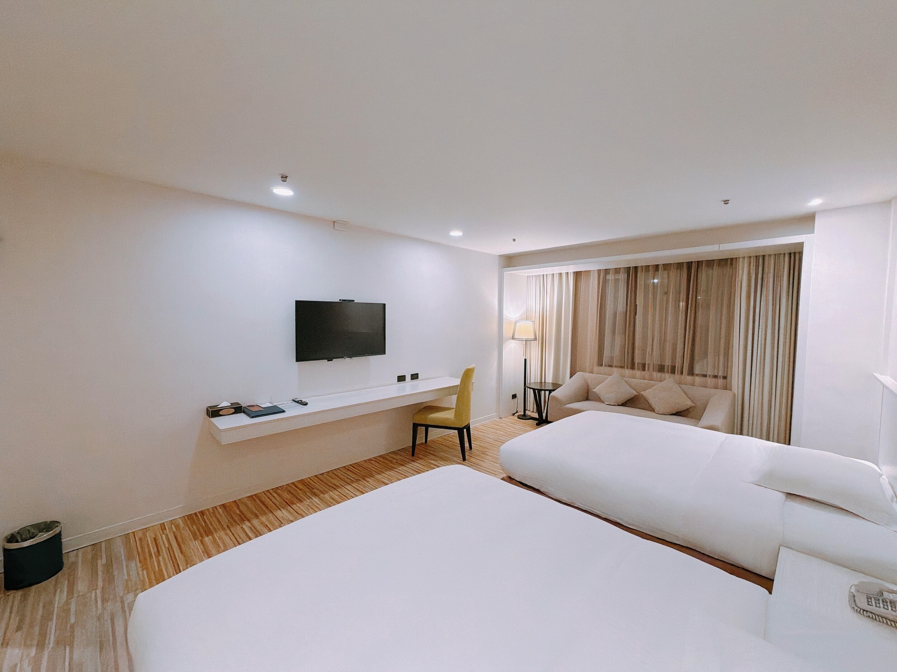 Une chambre d’hôtel avec un grand lit, un bureau avec une chaise, un téléviseur fixé au mur et une fenêtre avec des rideaux.