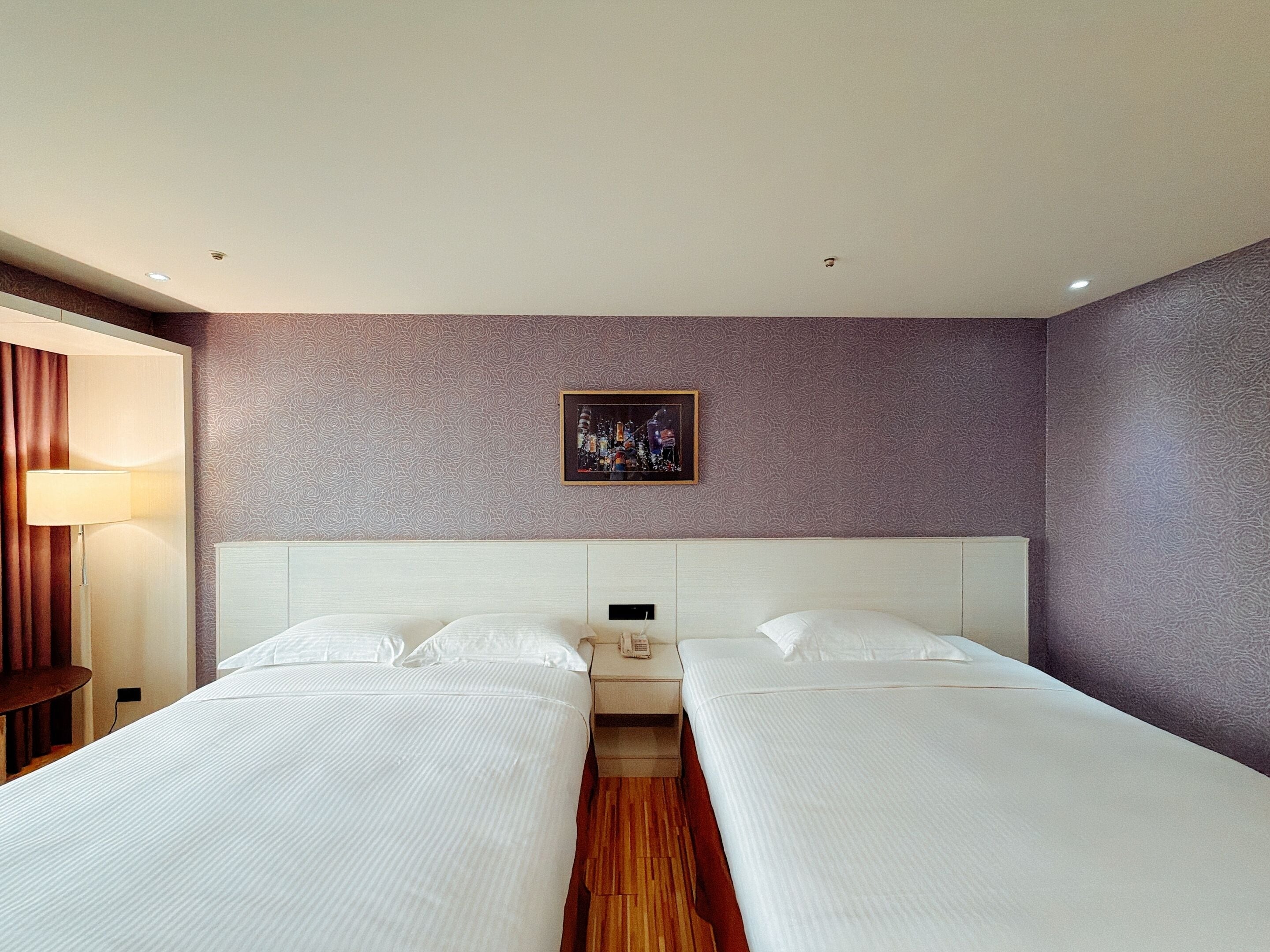 A hotel room with two beds, a nightstand, a lamp, and a framed picture on the wall.