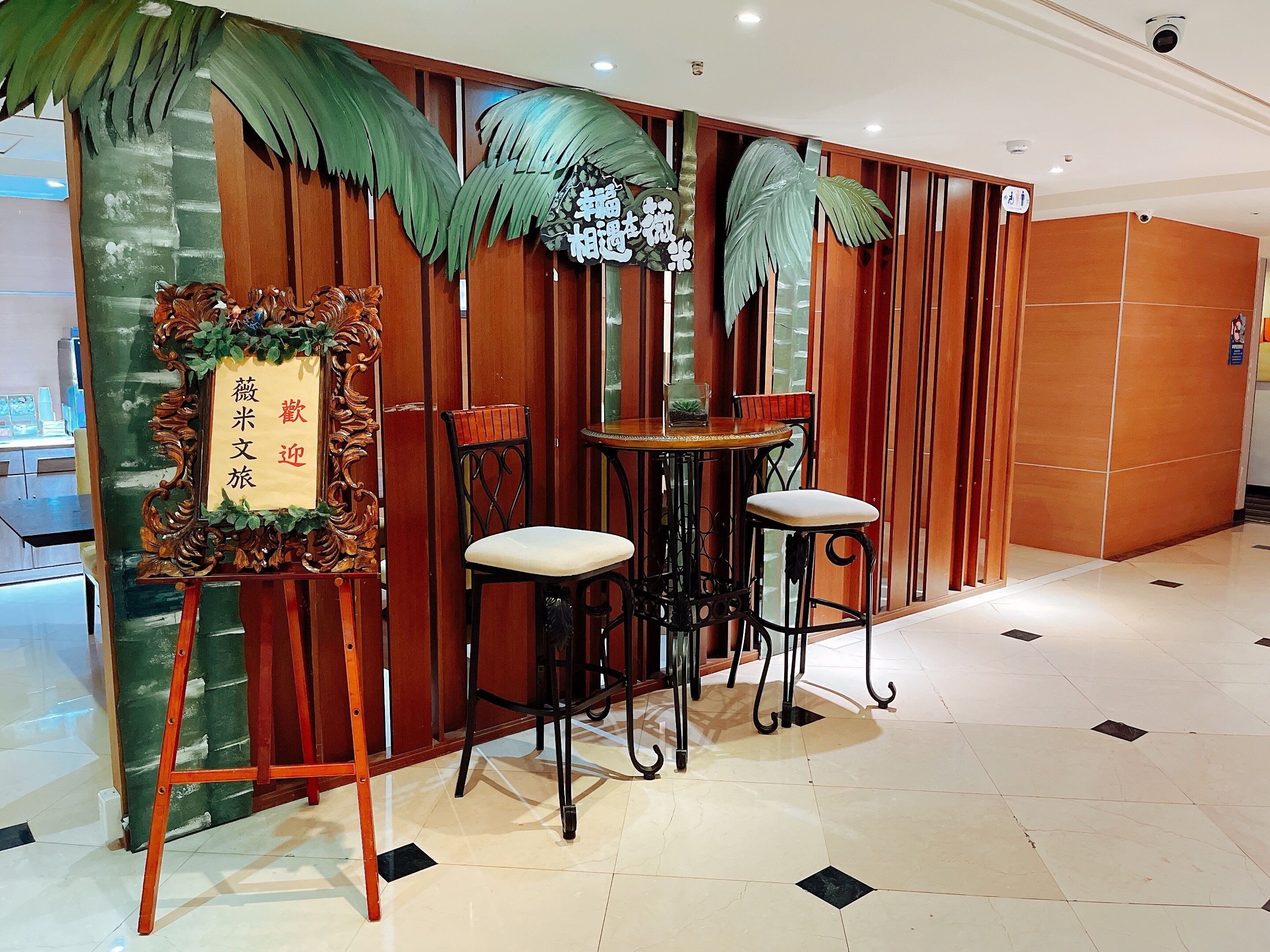 A reception area with a wooden reception desk, two chairs, a small table, and decorative palm leaves.