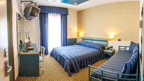 Hotellihuone, jossa on sänky, työpöytä, jossa on televisio, tuoli ja pieni pöytä, jossa on kukkia.