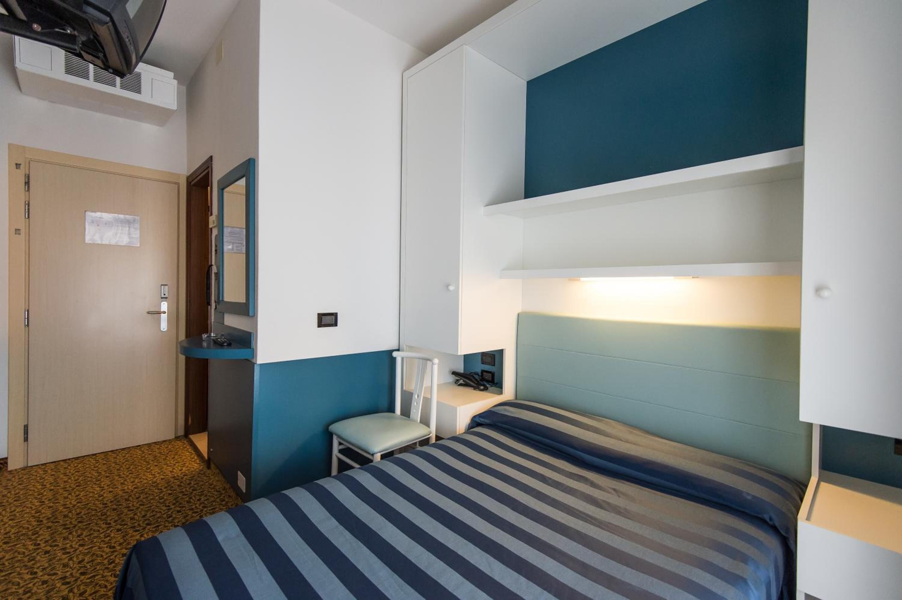Une chambre d’hôtel comprenant un lit, un bureau, une chaise, une armoire et un miroir.