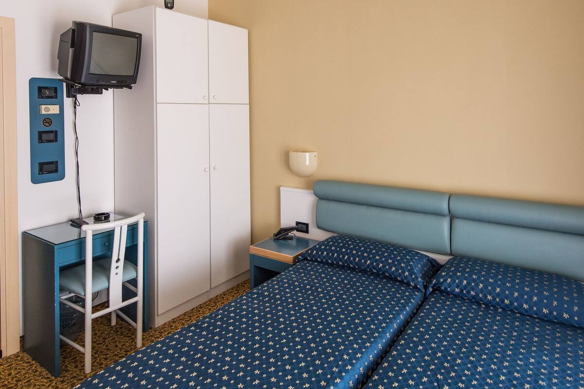 A hotel room with a bed, a desk with a television, a wardrobe, and a ceiling with recessed lighting.