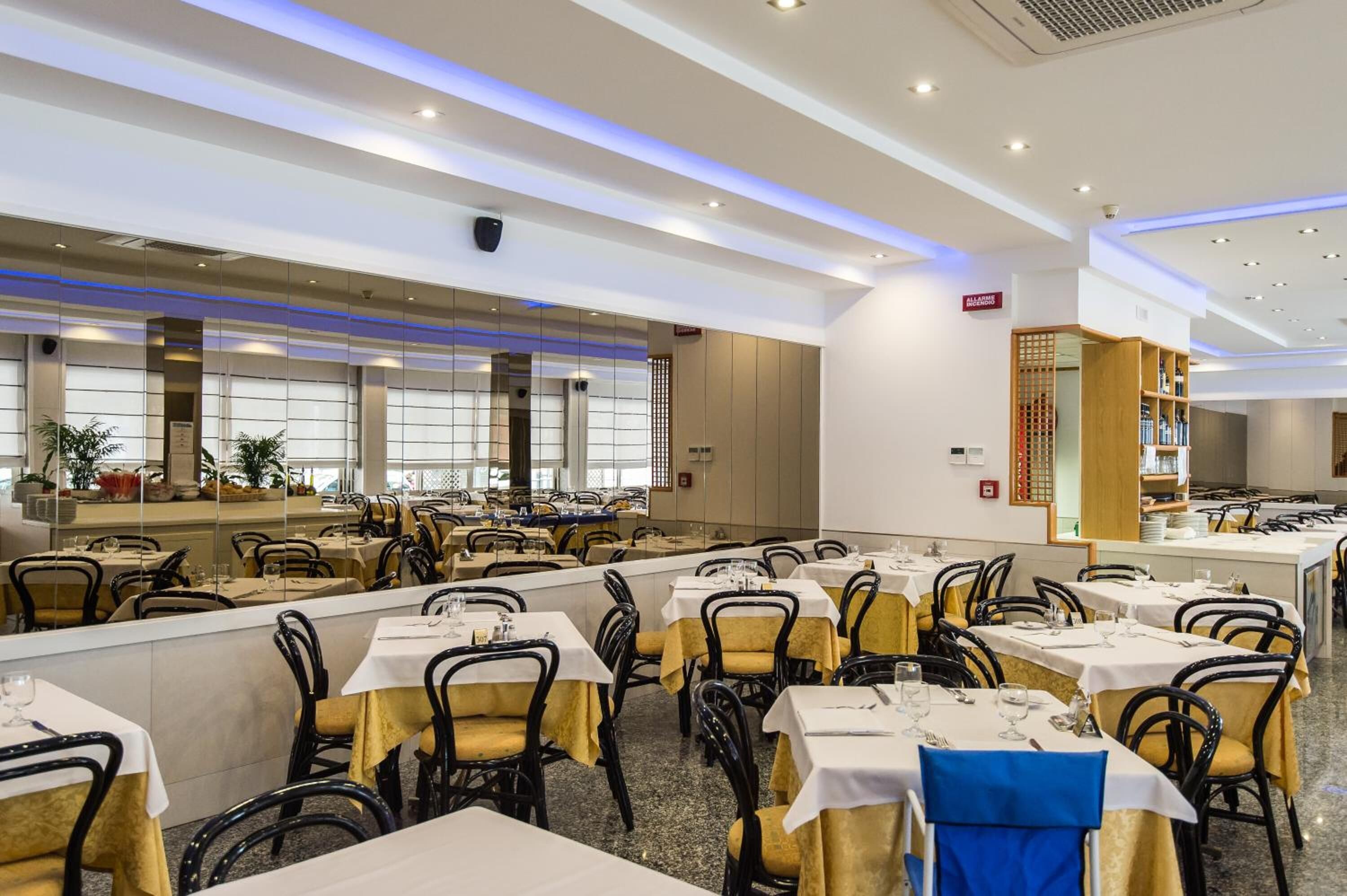 A spacious dining area with multiple tables and chairs, a central counter, and a large window providing natural light.