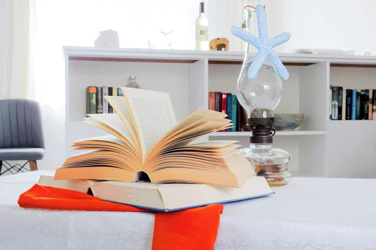 An open book on a table with a red ribbon, a blue starfish decoration, and a clear bottle with a light bulb.