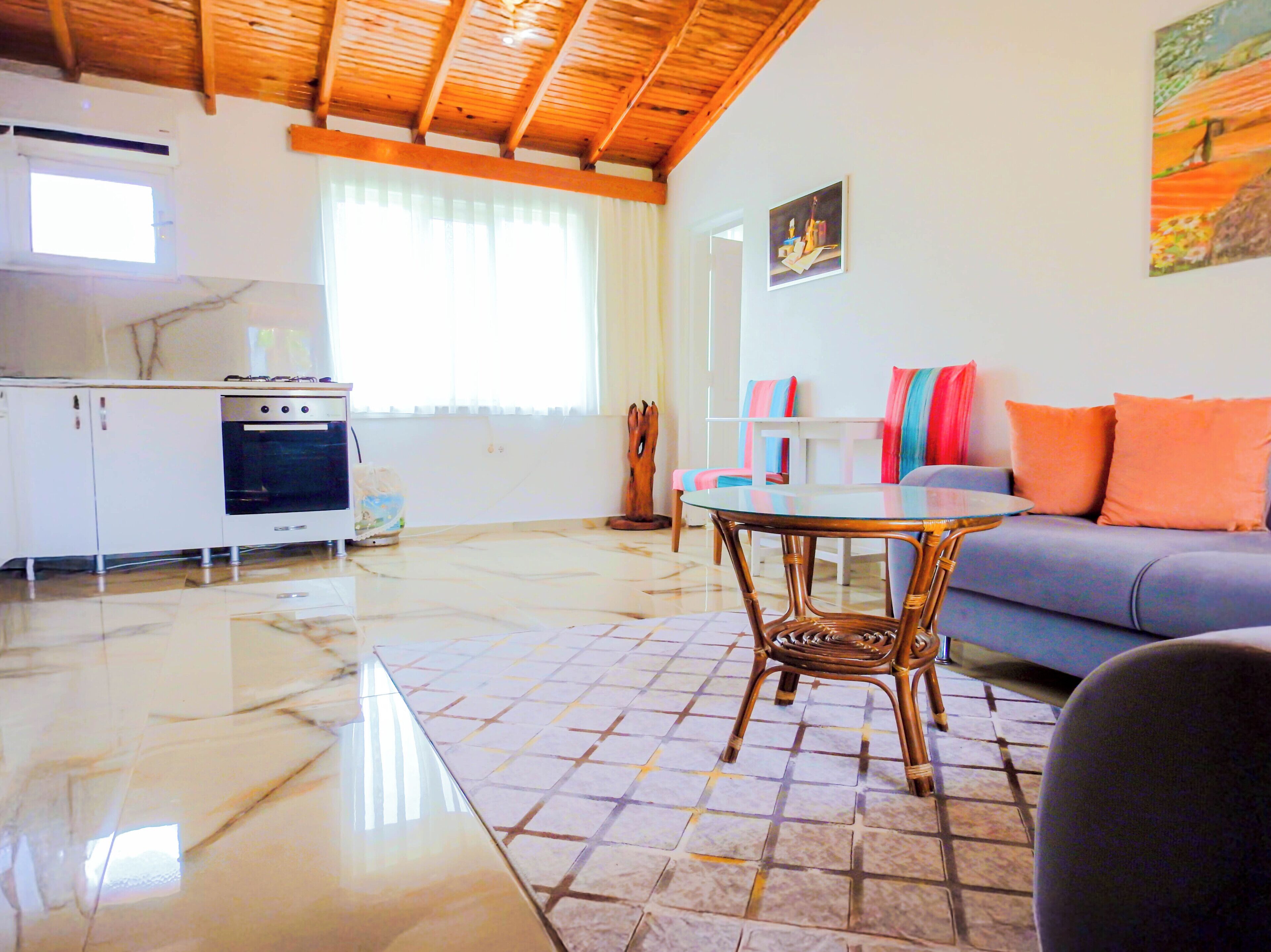 Amplia sala de estar con piso de baldosas, cocina con estufa, mesa de comedor y sofá con cojines de colores.