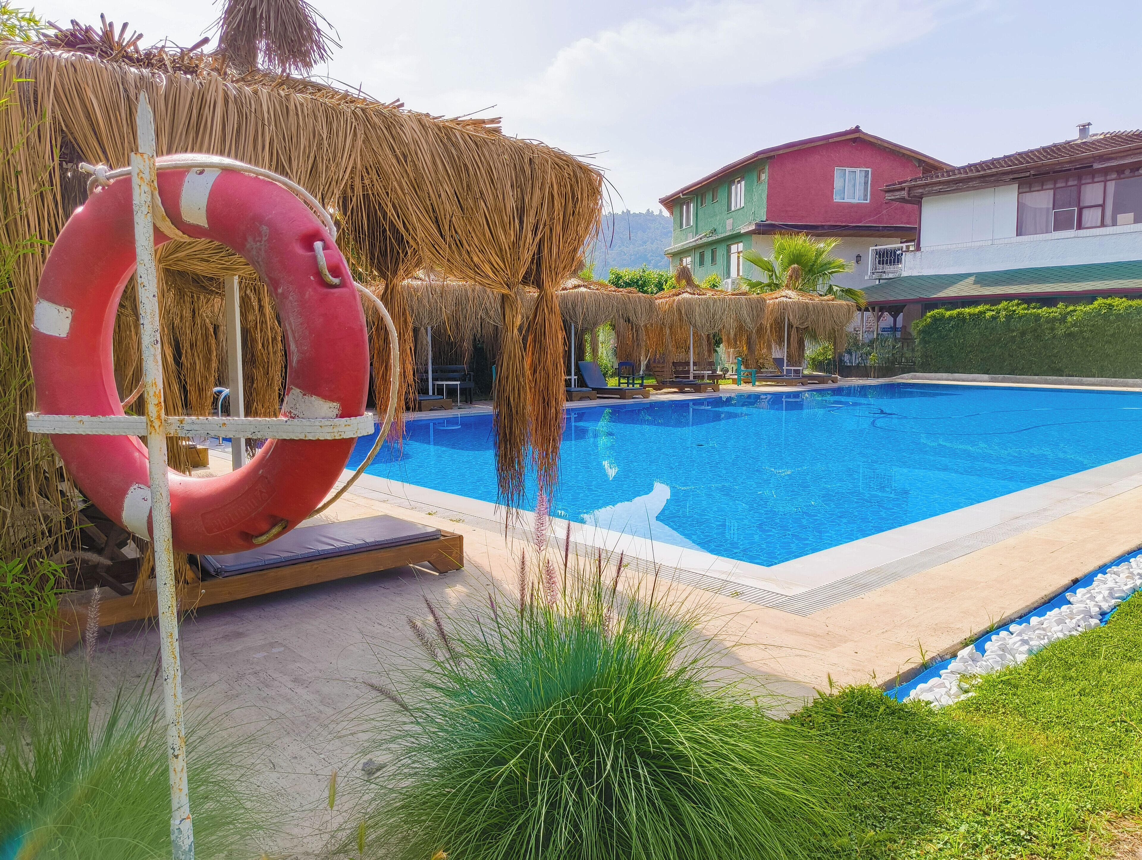 Una piscina con un flotador salvavidas, sombrillas de paja y sillas de descanso.
