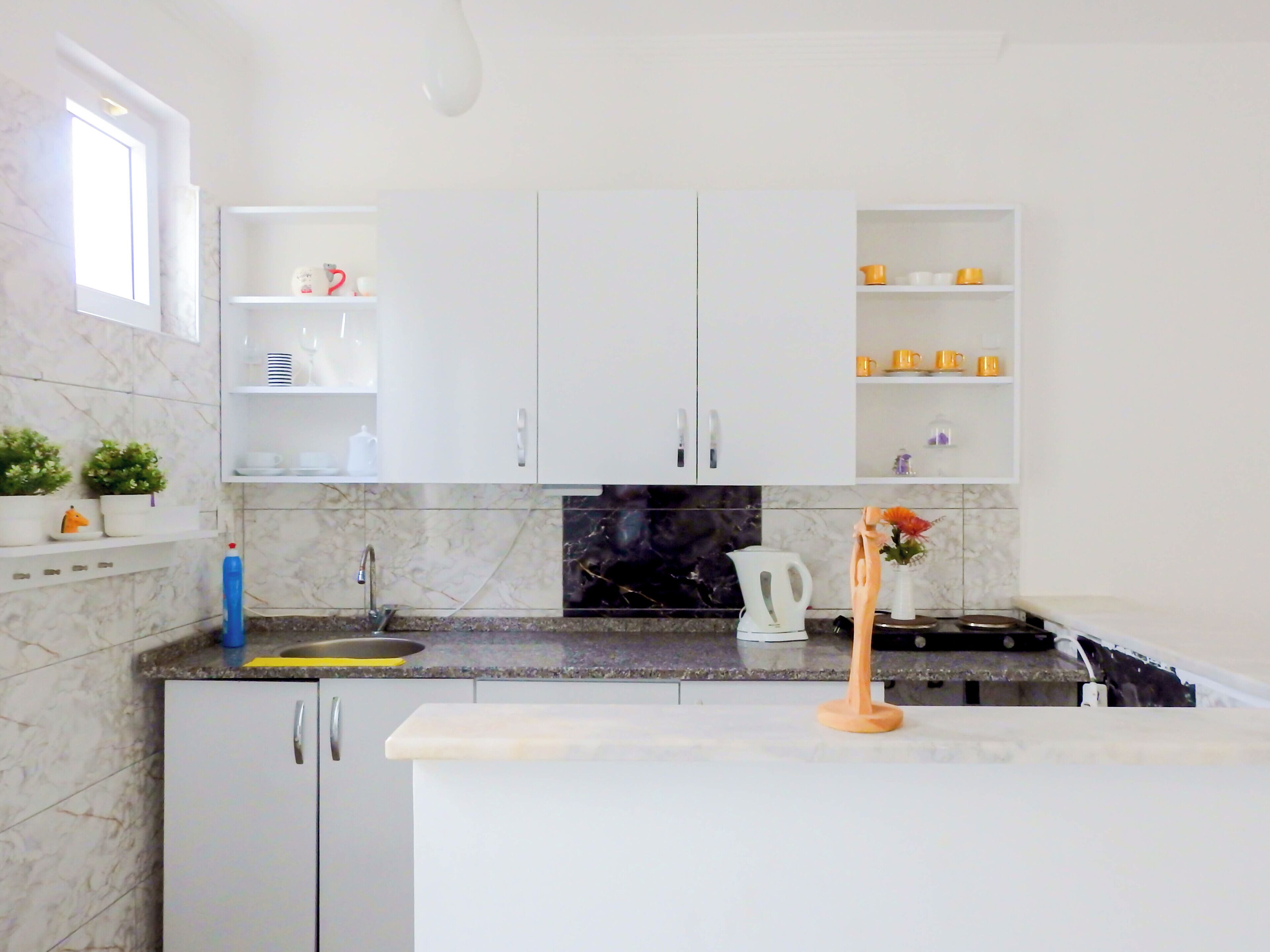Una cocina moderna con armarios blancos, salpicadero de mármol y encimera de granito.