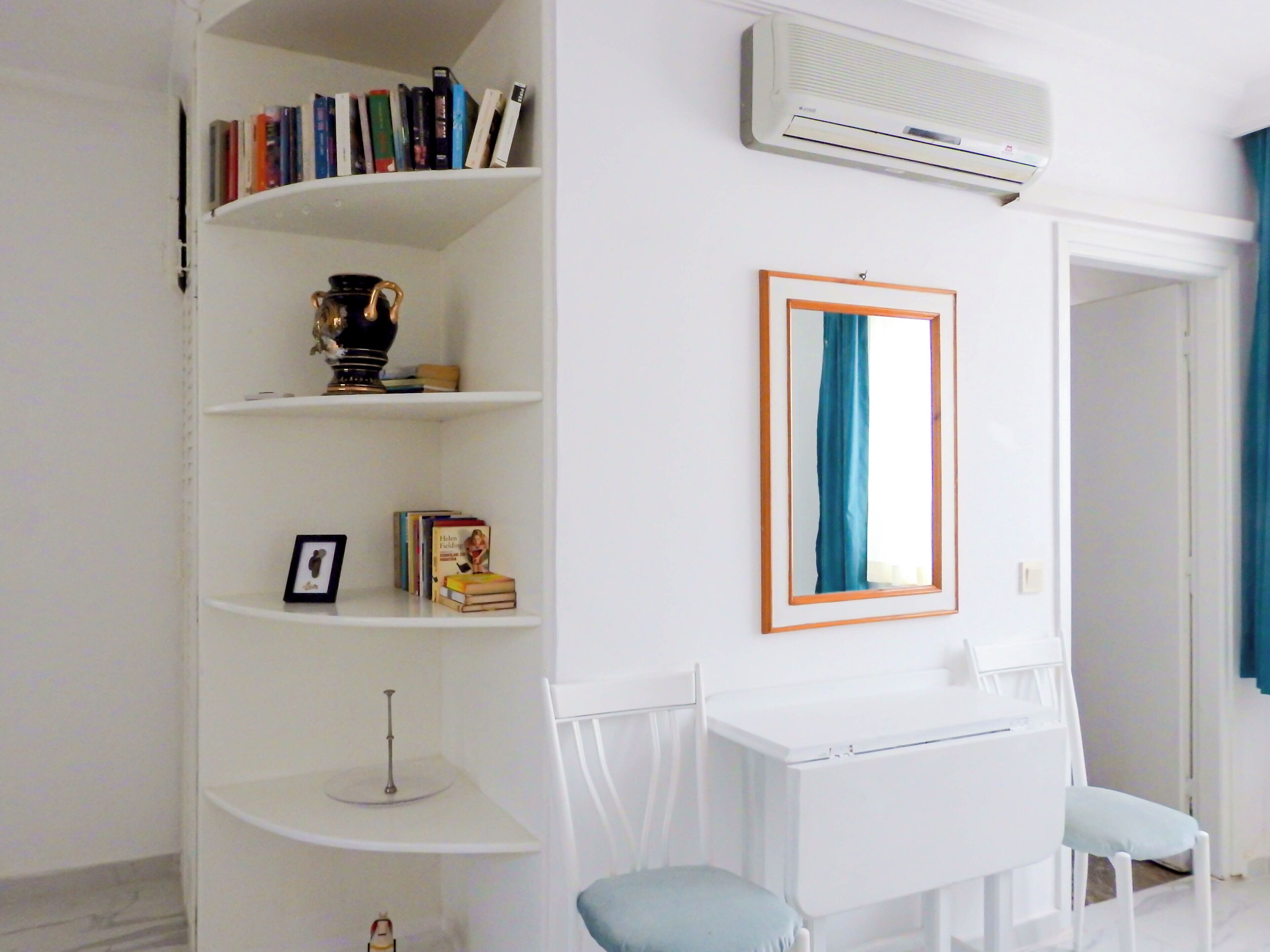 A room with a white desk, two chairs, a bookshelf, and an air conditioning unit.