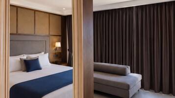 A modern hotel room with a bed, a sofa, a nightstand, and a large window with curtains.