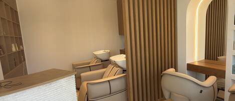A modern spa room with a massage chair, a wooden partition, and a reception desk.
