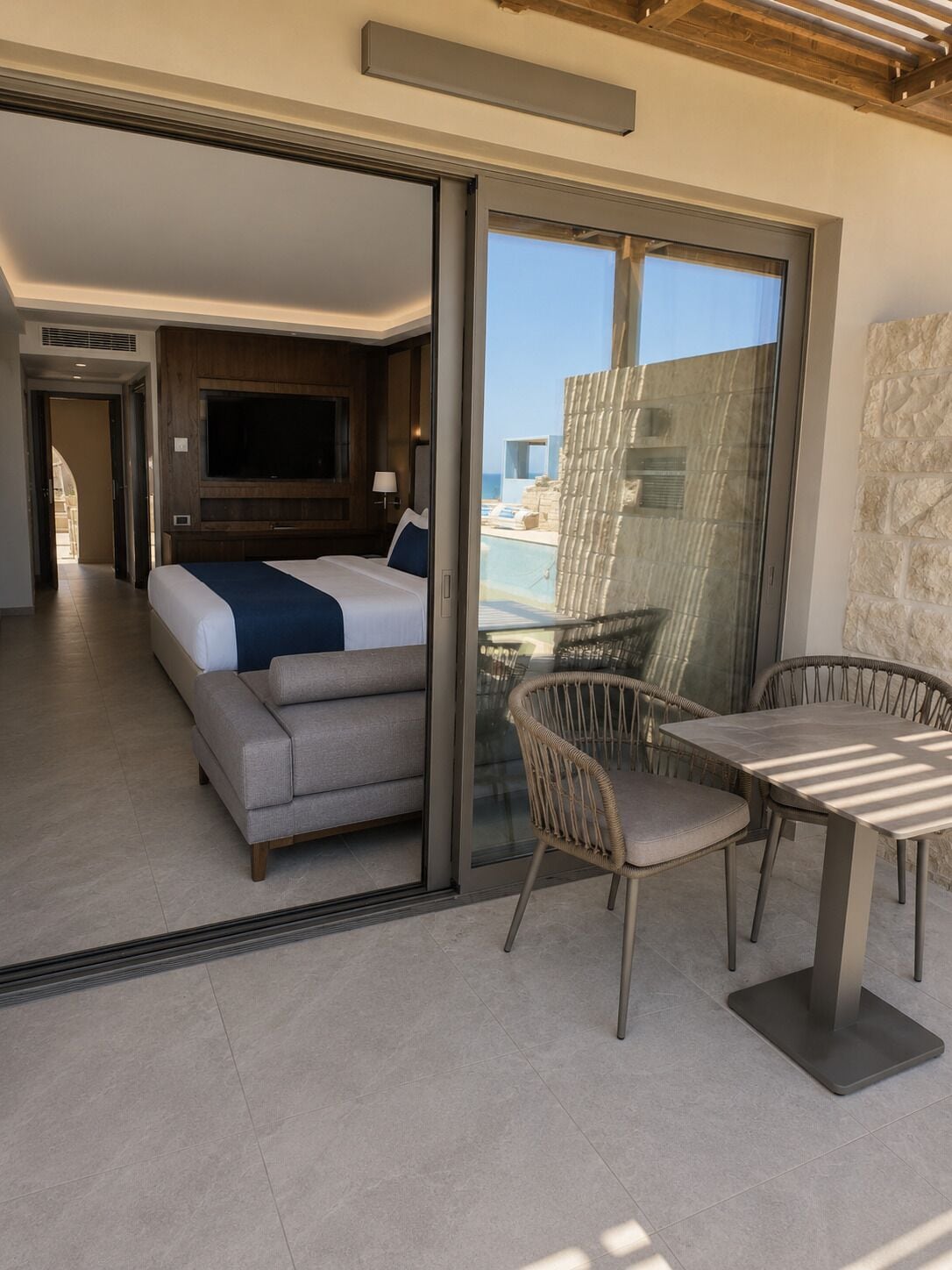 A modern hotel room with a bed, a TV, a sofa, a dining table, and a view of the sea.