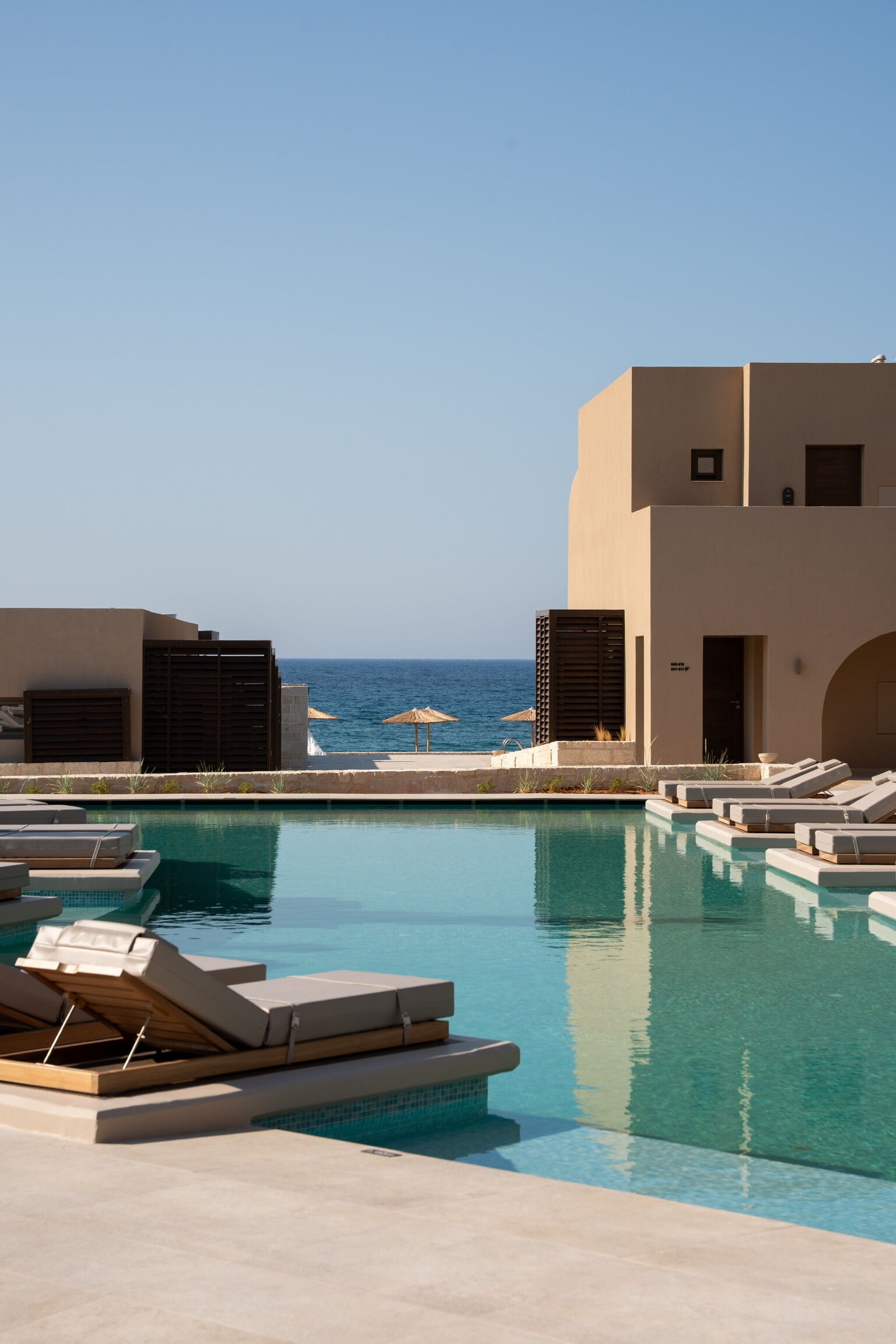 A pool area with lounge chairs, a view of the sea, and a building with a flat roof.