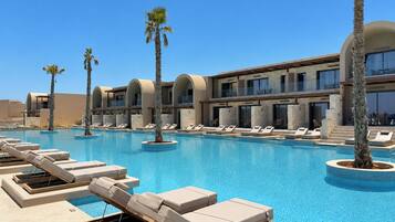 A resort pool area with sun loungers, palm trees, and a modern building with balconies.