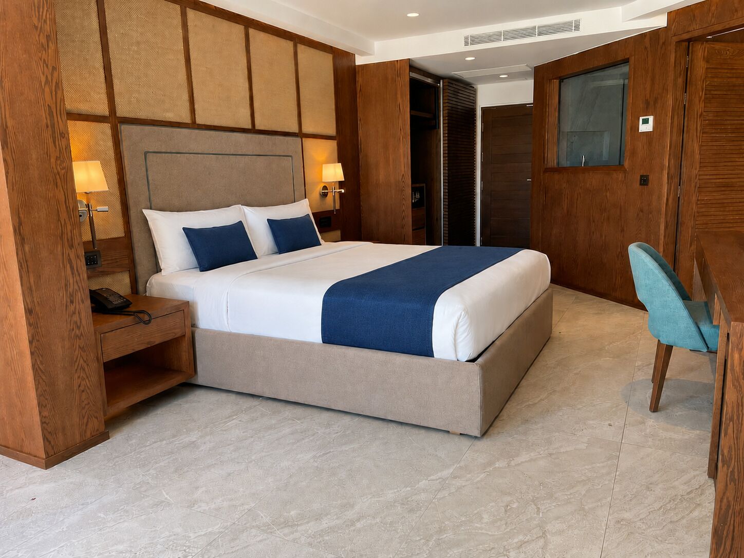 A hotel room with a large bed, bedside lamps, a wooden wardrobe, and a chair.