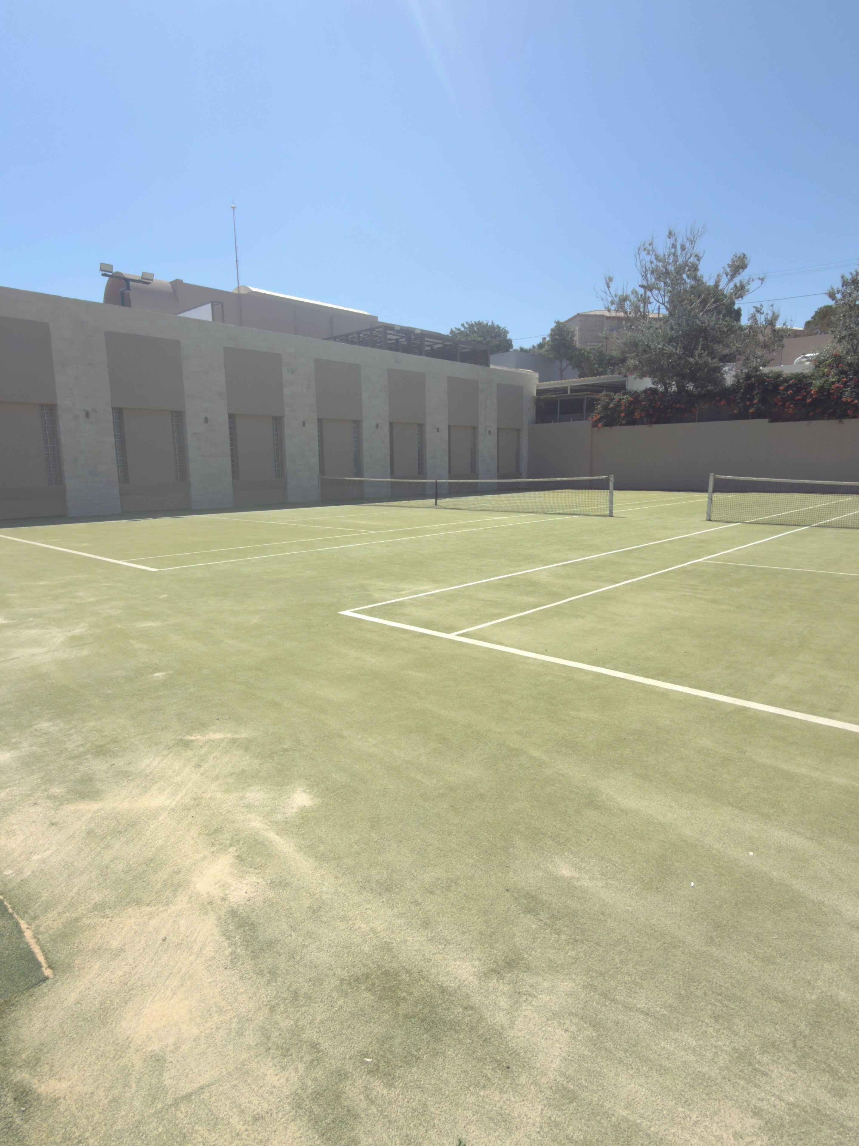 An outdoor tennis court with a net, surrounded by buildings and trees.