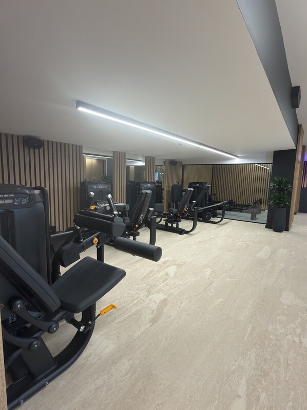 A gym with exercise equipment, a mirror wall, and a plant. - Nana Royal Premium Resort & Spa (Hersonissos)