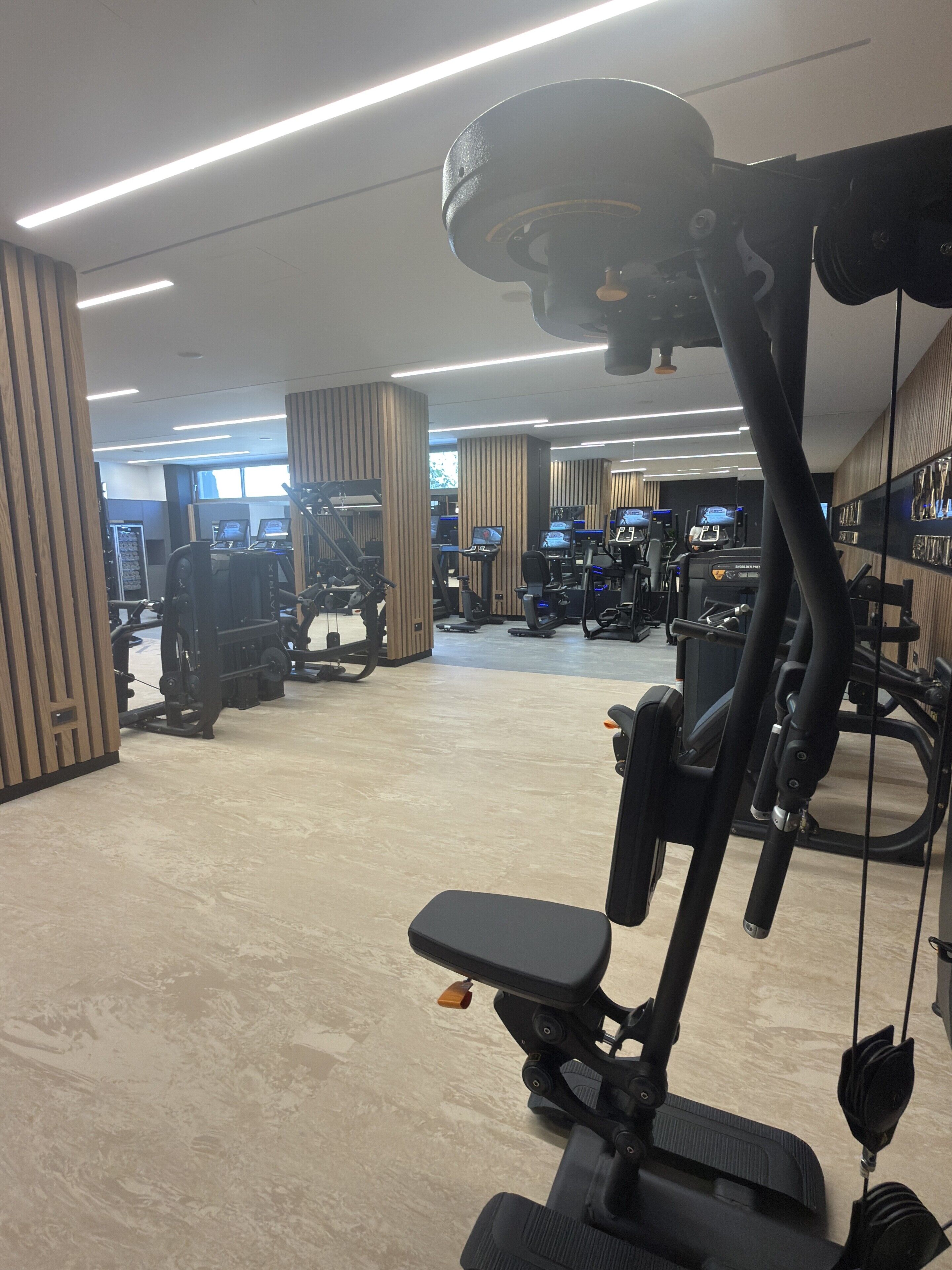 Un gimnasio con equipo de ejercicio, paneles de madera y un techo con luces lineales.