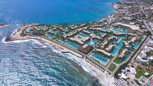 An aerial view of a coastal resort with multiple swimming pools, beachfront areas, and a mountainous backdrop. - Nana Royal Premium Resort & Spa (Hersonissos)