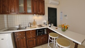 A kitchen with wooden cabinets, a white countertop, a toaster, a sink, and a white refrigerator. - Pelagos Apartments (Corfu)