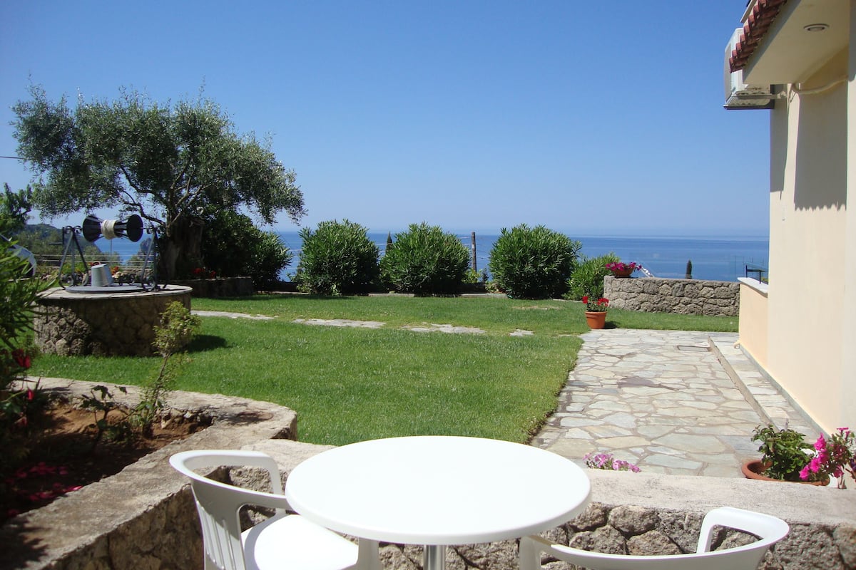 Un patio con una mesa y sillas de piedra, un muro de piedra y vista al mar.