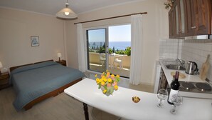 A bedroom with a bed, a bedside table with a lamp, a window with curtains, and a view of the sea. - Pelagos Apartments (Corfu)