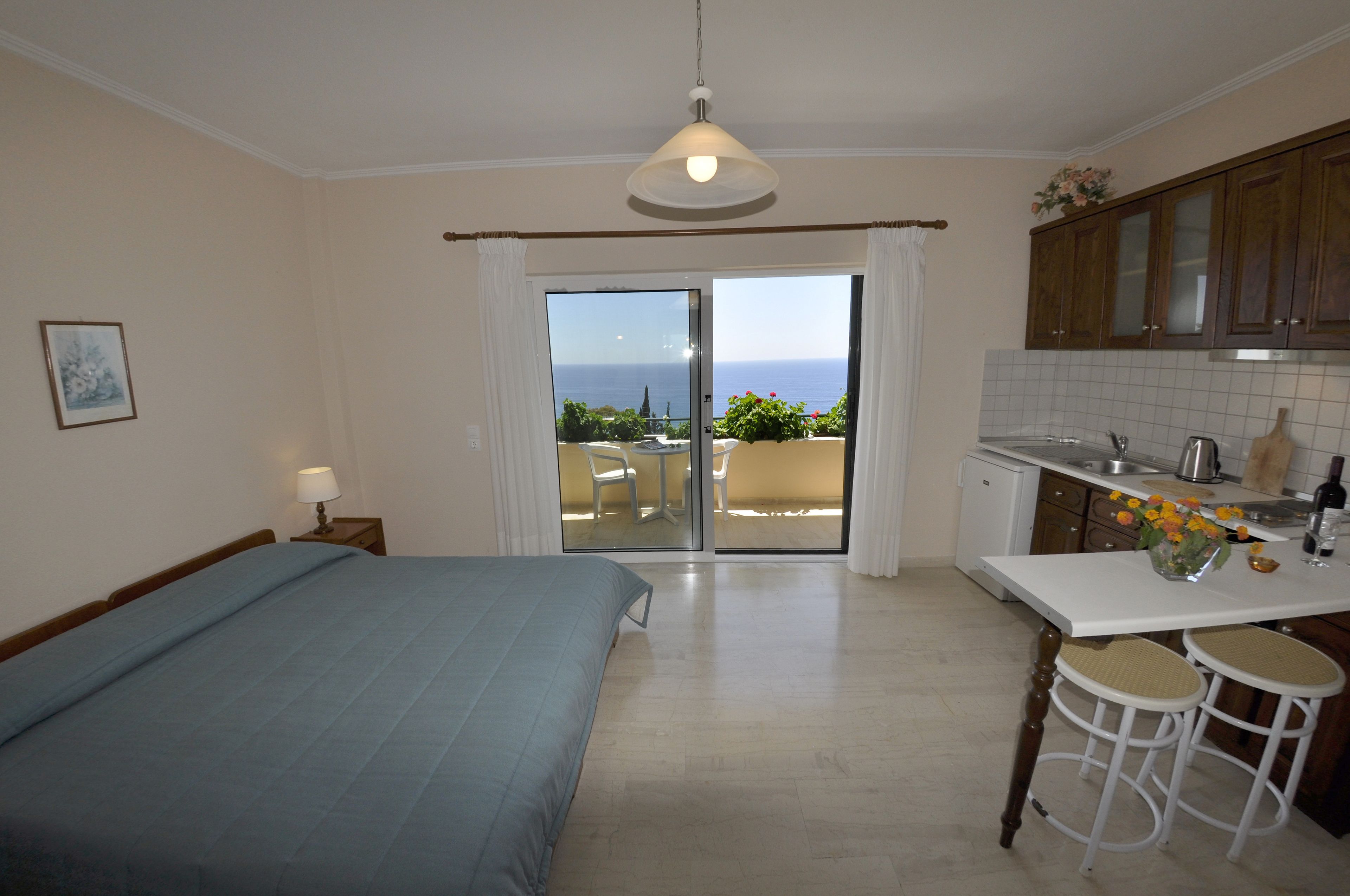 A bedroom with a bed, a nightstand, a lamp, and a view of the balcony.