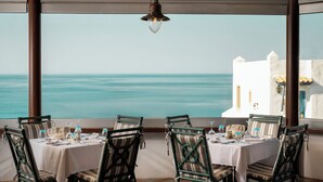 A table set for dining with chairs, a hanging light fixture, and a view of the sea. - Canvas by Mitsis Cretan Village (Hersonissos)