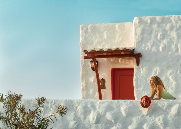 Un edificio con fachada blanca y puerta roja, una pérgola de madera y una placa con un número.