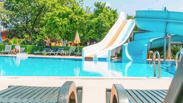 Relax by the pool surrounded by lounge chairs and umbrellas, with a water slide leading into the pool.
