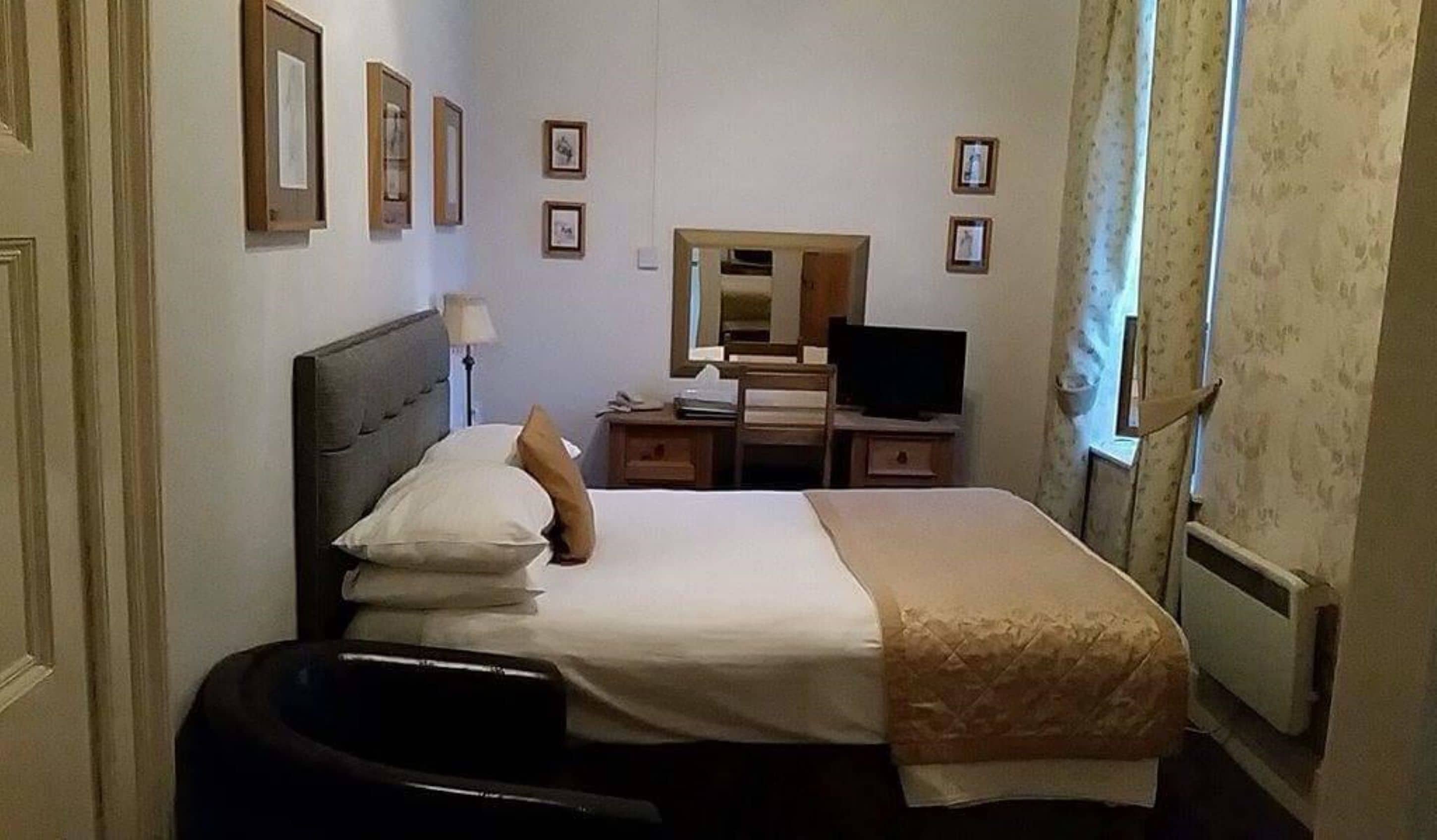 A hotel room with a bed, a desk, a chair, a television, and framed pictures on the wall.