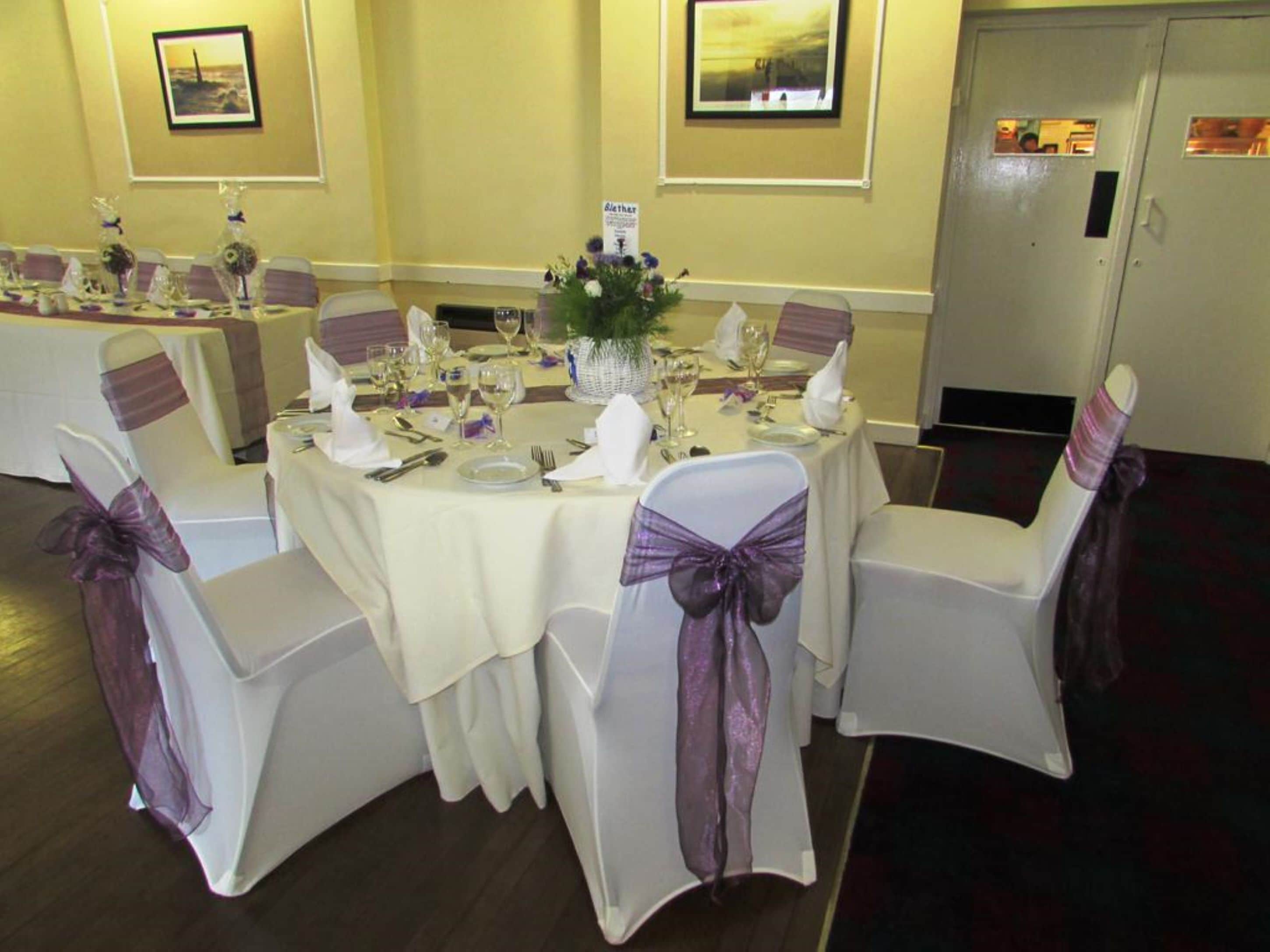 A banquet table set for a formal event with white tablecloths, purple sashes, and glassware.