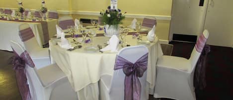 A banquet table set for a formal event with white tablecloths, purple sashes, and glassware.