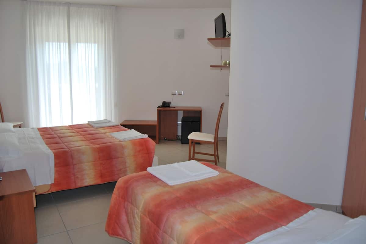 Quarto de hotel com duas camas, uma escrivaninha, uma cadeira e uma televisão em uma estante.