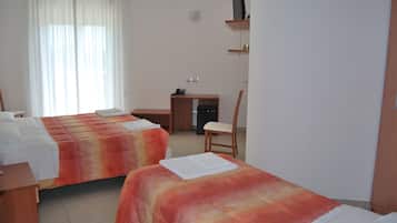 Habitación de hotel con dos camas, un escritorio, una silla y un televisor sobre una estantería.