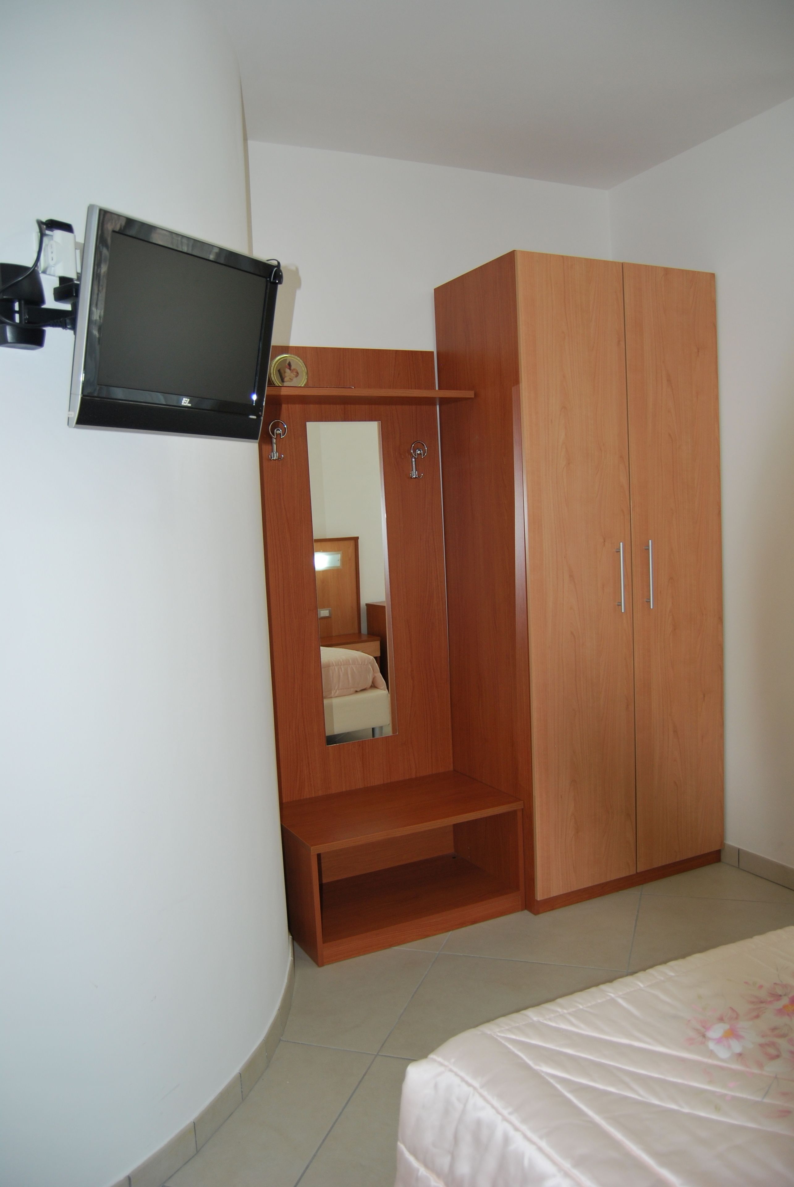 Ein Schlafzimmer mit einem Holzkoffer, einem an der Wand befestigten Fernseher und einem Bett mit Blumenmuster-Bettwäsche.
