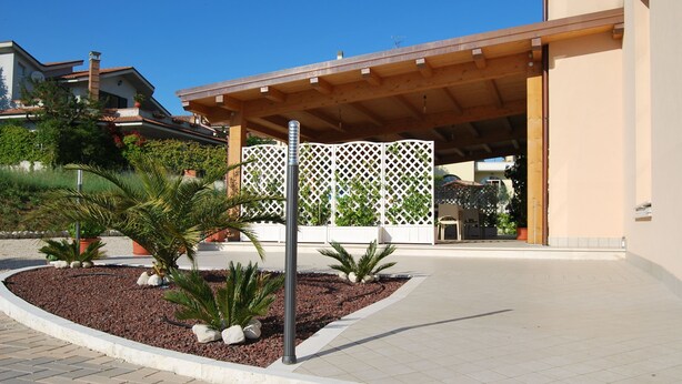 Un edificio moderno con un acceso cubierto, un jardín ajardinado con palmeras y una valla blanca de celosía.