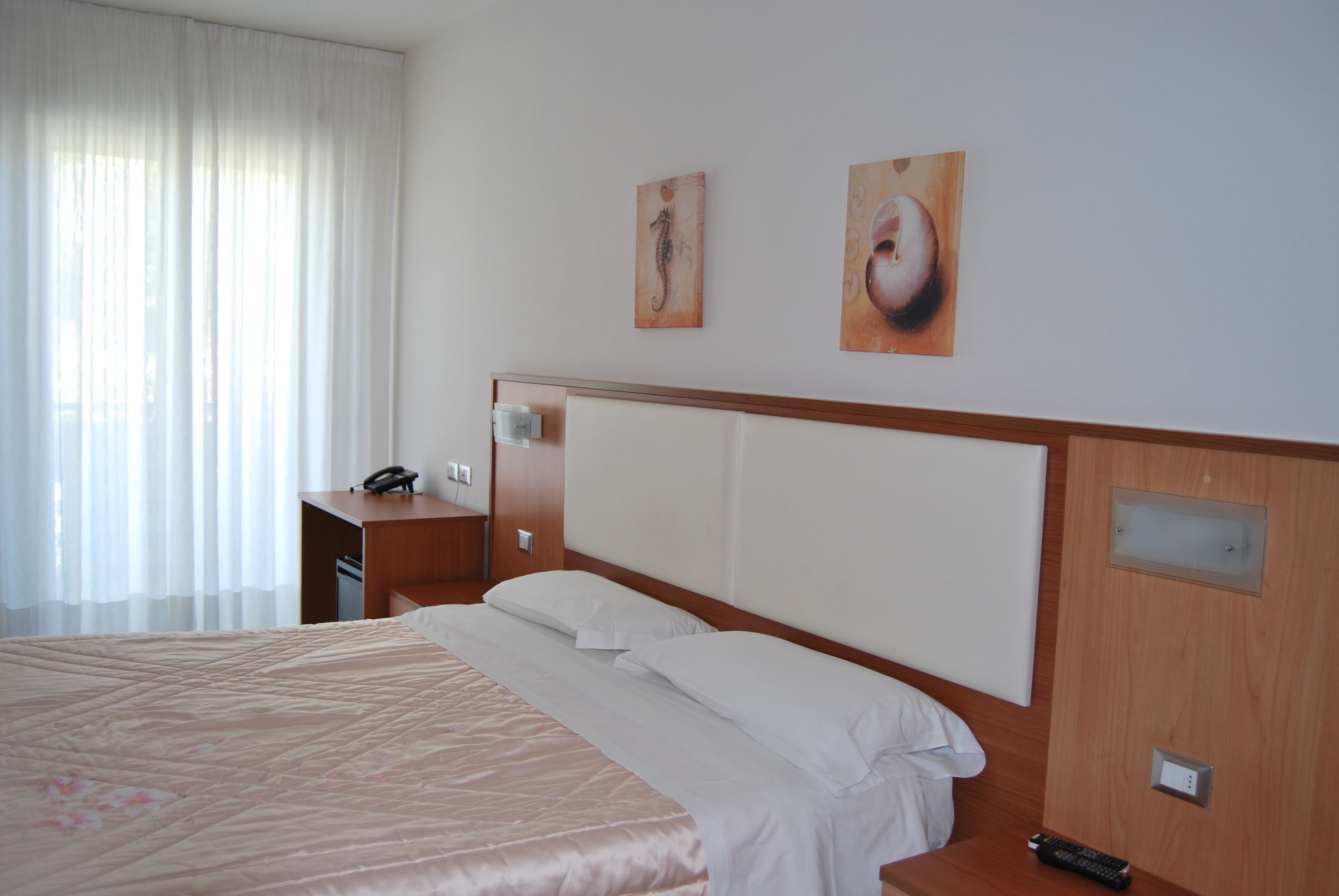 Une chambre d’hôtel avec un grand lit, une table de chevet en bois, un bureau et deux tableaux au mur.