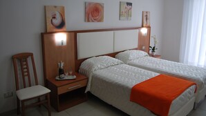 Habitación de hotel con dos camas, una mesita de noche de madera, una silla y una obra de arte en la pared.