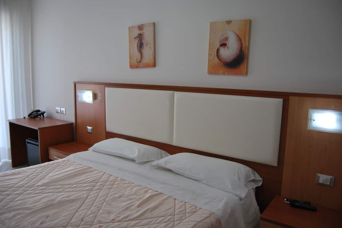 Quarto de hotel com uma cama grande, cabeceira de madeira, mesa de cabeceira com telefone e uma obra de arte na parede.