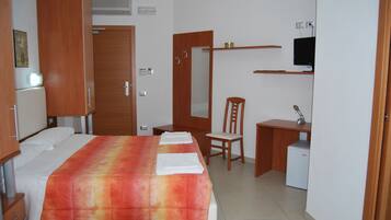 Una habitación de hotel con una cama, un escritorio, una silla, un televisor y un refrigerador pequeño.