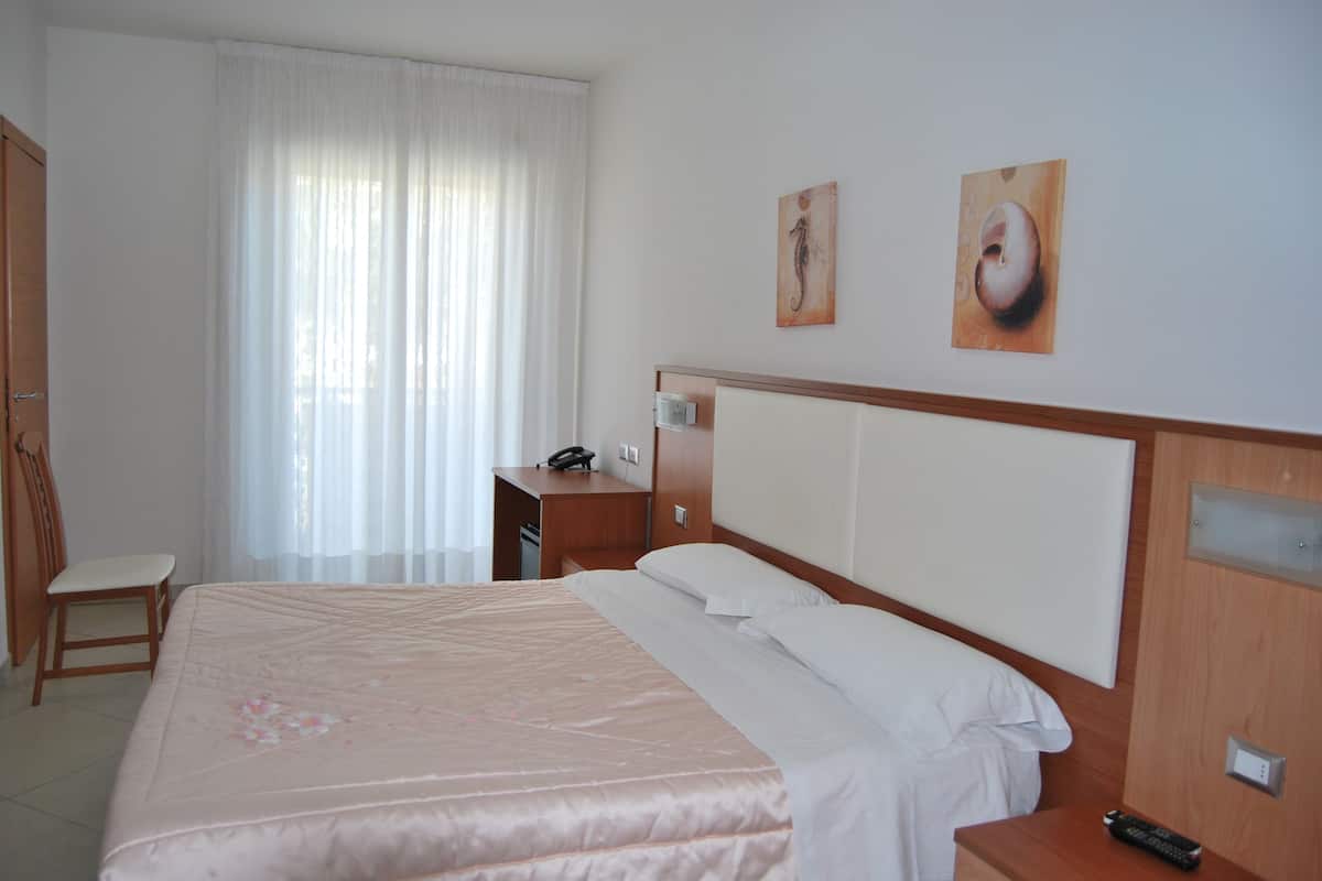 Quarto de hotel com cama, escrivaninha, cadeira e janela com cortinas.