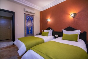 A hotel room with two beds, each with green and white bedding, a nightstand with a phone, and a wall-mounted light fixture. - Atlantic Hotel Agadir (Agadir)