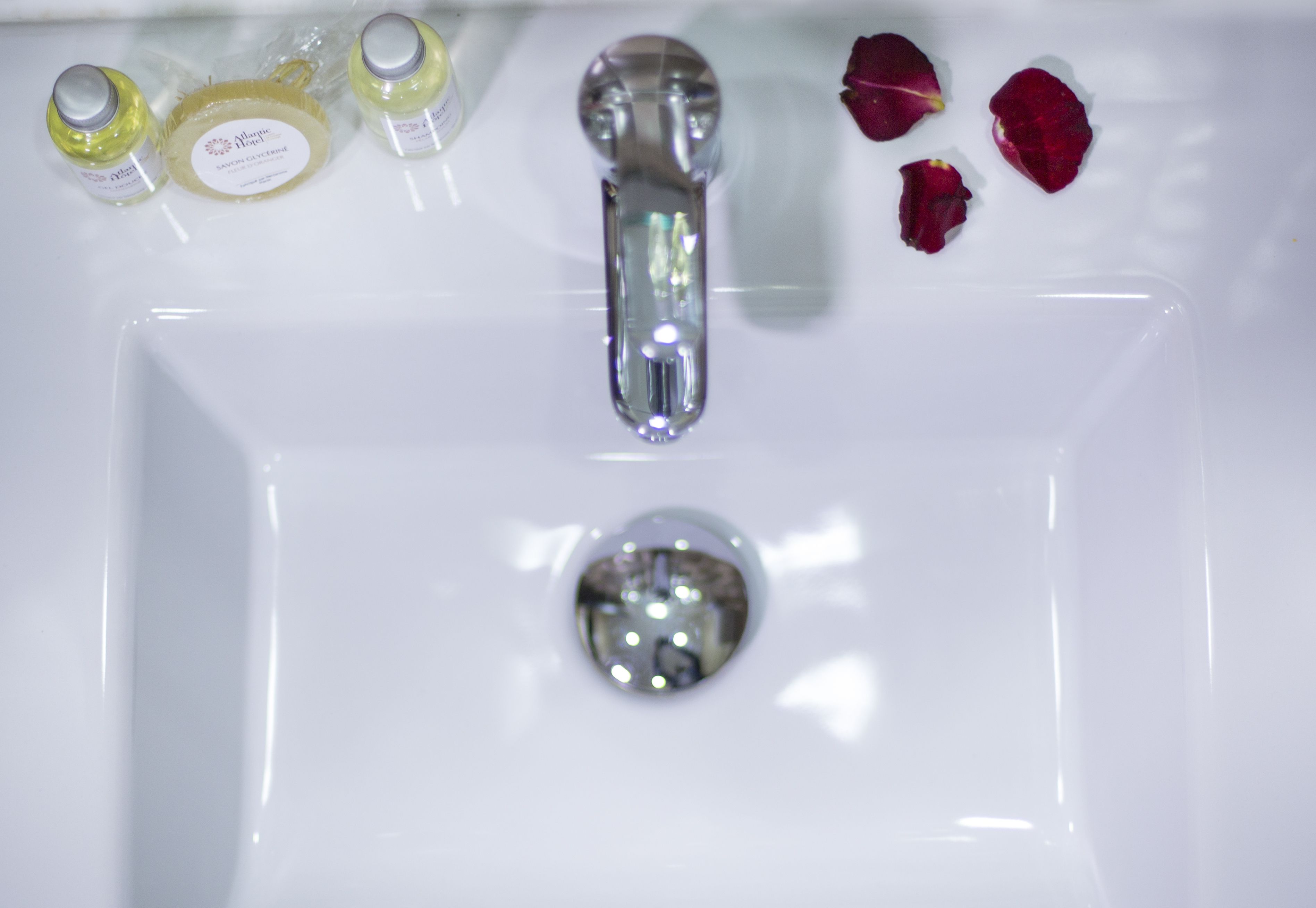 Un lavabo de bany blanc amb un aire cromat, dues ampolles de xampú i pètals de rosa.