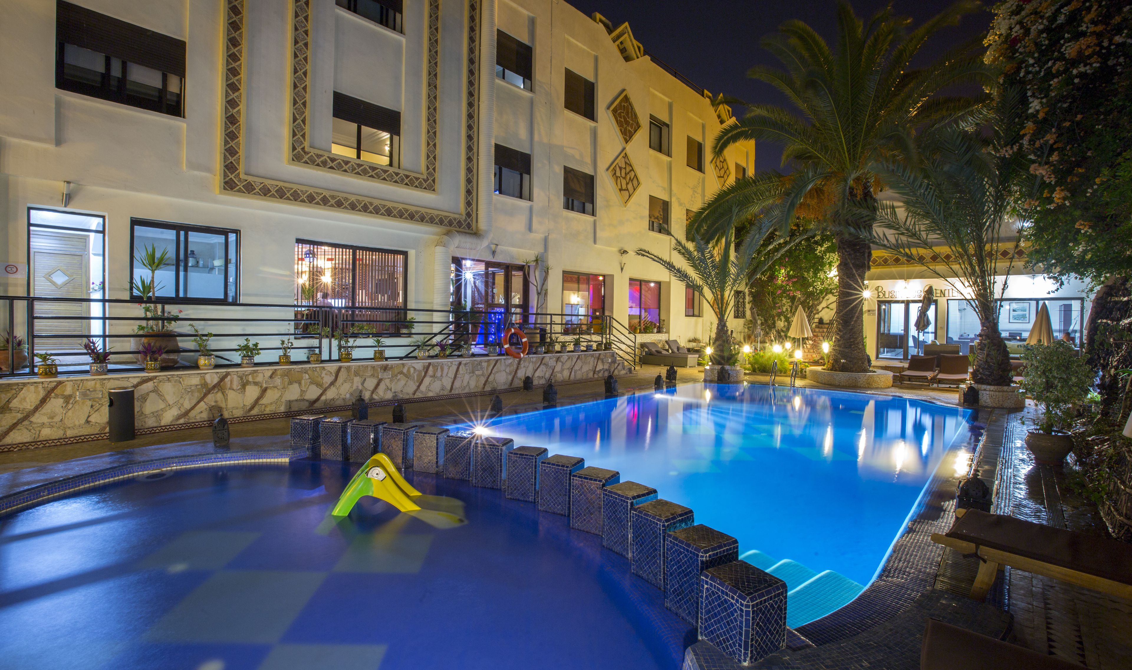 Una piscina con un flotador salvavidas, sillas de descanso y un edificio con múltiples ventanas y balcones.
